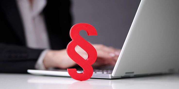 Paragraphenzeichen vor an einem Laptop tippenden Händen